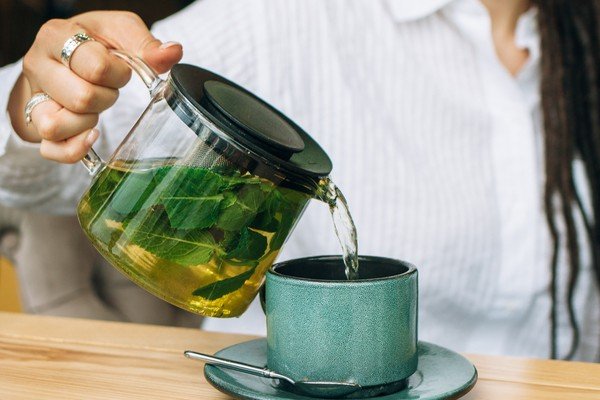 Jarra de vidro com chá verde abastece xícara de vidro-Metrópoles