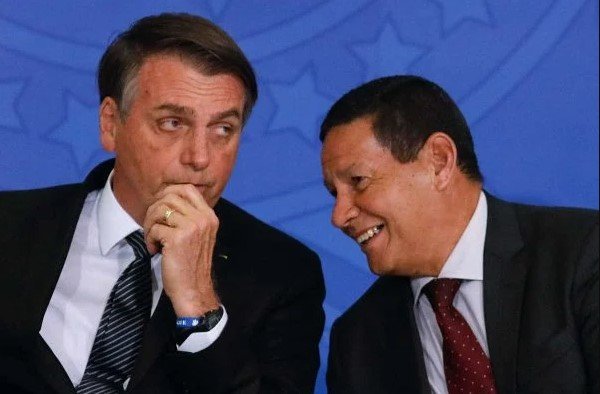 Bolsonaro e Mourão conversam ao pé da orelha no Planalto. Eles vestem terno e gravata e tem cabelos escuros - Metrópoles