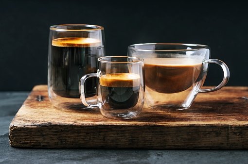 três xícaras de vidro contendo café dentro. Foto com fundo preto