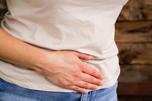 Woman dressed in white blouse and jeans presses her stomach with her hands - Metropolis