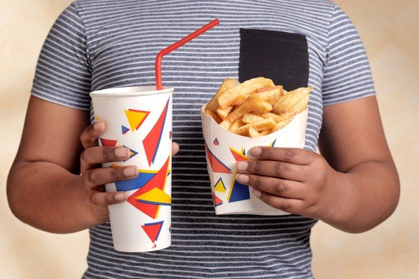 Man in striped shirt holds package with chips and glass of soda - Metropolises