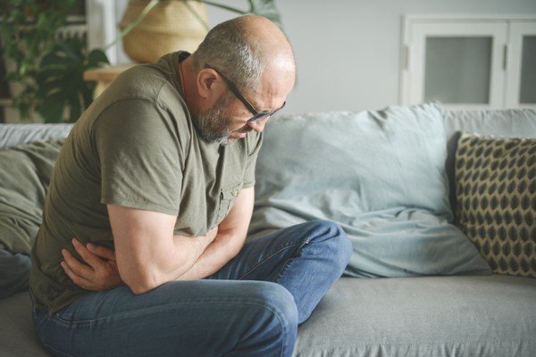 Man Sitting On Couch Squeezes His Belly With Hands - Metropolises