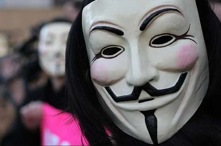 Pessoa com máscara dos Anonymous em manifestação olha para a câmera - Metrópoles