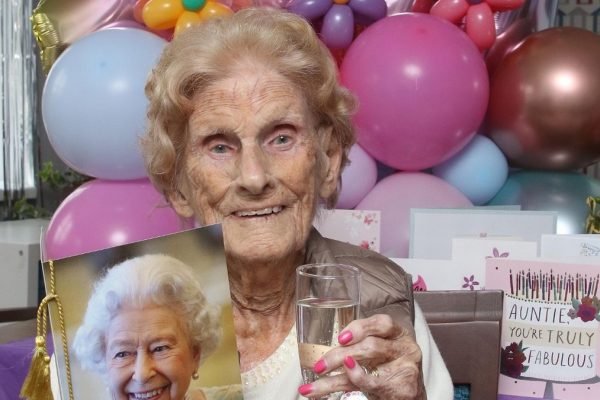 Mulher idosa segurando taça de bebida com balões de aniversário atrás