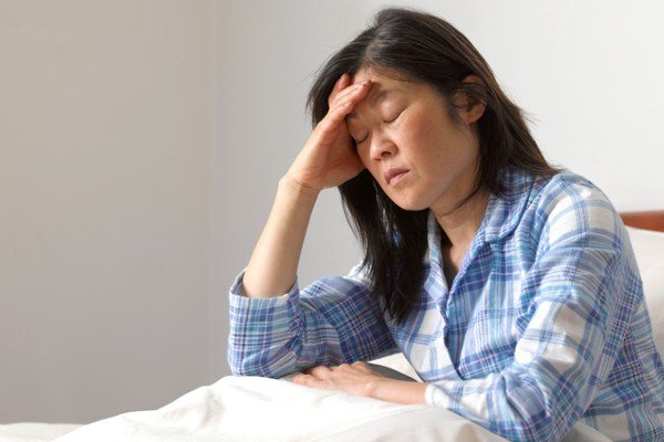 Woman sitting on the edge of the bed appears to be ill.  She puts her hand on her forehead and has her eyes closed - Metropolis