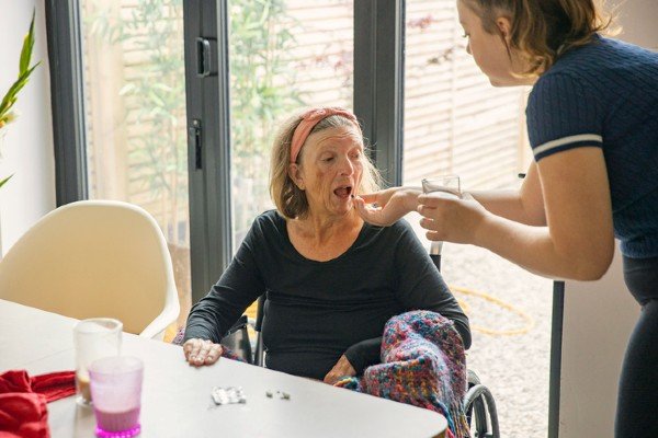 An elderly woman gets medicine into a nurse's mouth