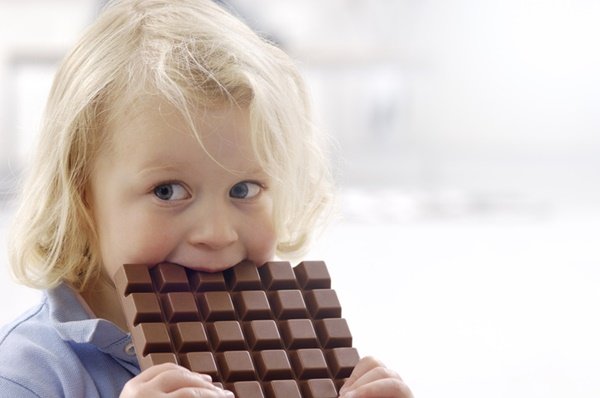 Child eating candy.  She has light hair and wears a light blouse