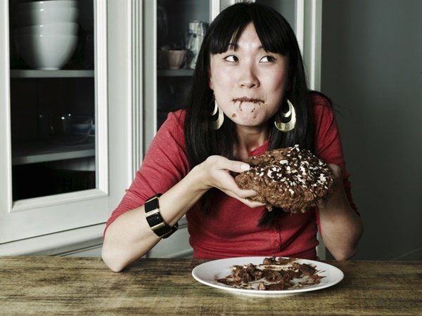 Woman holding the whole cake with both hands.  She has black hair and wears a red shirt.