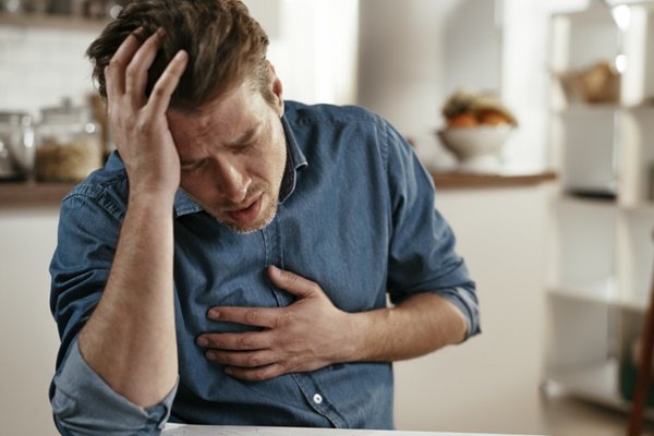 Man with one hand on his head and the other on his chest as if he is feeling sick