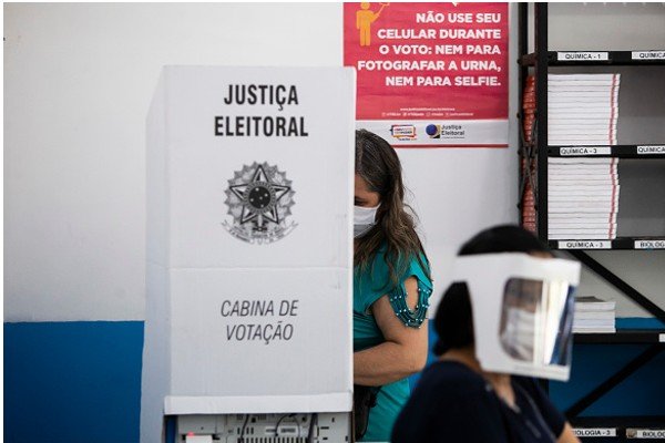 Mulher veste blusa verde e usa cabine de votação-Metrópoles