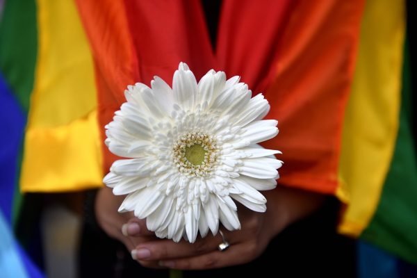 mulher com a bandeira LGBT segurando uma flor