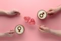 Fundo rosa com dois cafés com símbolos femininos e masculinos. No meio, dois pirulitos em formato de coração