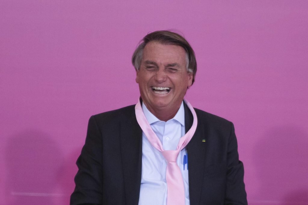 Jair Bolsonaro ri em cerimônia de comemoração do Dia da Mulher no Palácio do Planalto. Ele usa uma gravat rosa - Metrópoles