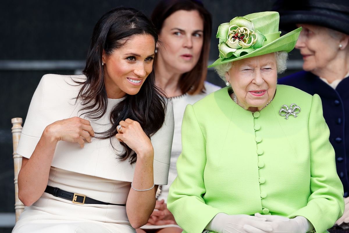 Foto colorida. Meghan Markle com roupas beges e a rainha Elizabeth com roupas verdes