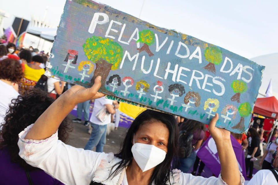 Em manifestação contra o machismo, racismo e lgbtfobia na Esplanada, em Brasília, uma mulher levanta cartaz com desenhos e os dizeres