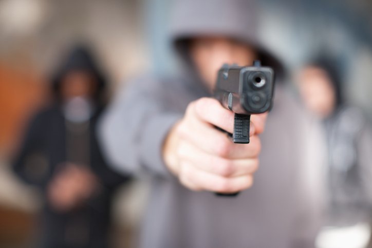 Pessoa encapuzada segurando uma arma preta nas mãos - metrópoles
