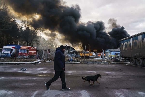 Homem anda por rua com cachorro após ataques aéreos russos na cidade de Kalynivka, Ucrânia. os escombros soltam muita fumaça e fogo - Metrópoles