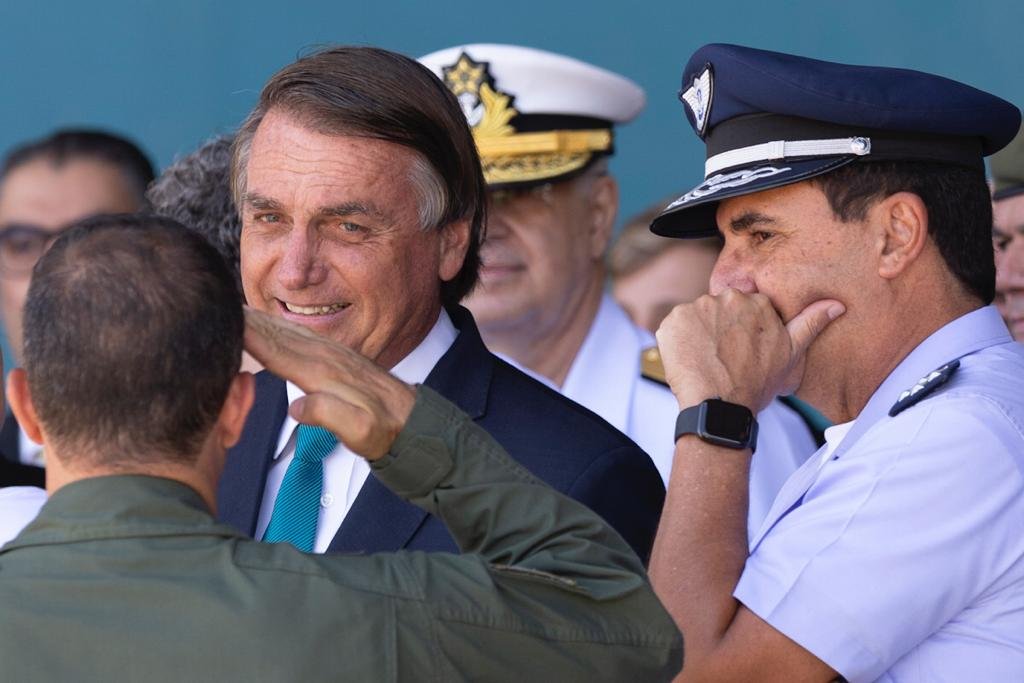 O presidente Bolsonaro recebe continência de um militar ao lado de Carlos Alberto Baptista Junior, comandante da Aeronáutica enquanto aguardam o avião com resgatados pousar - Metrópoles