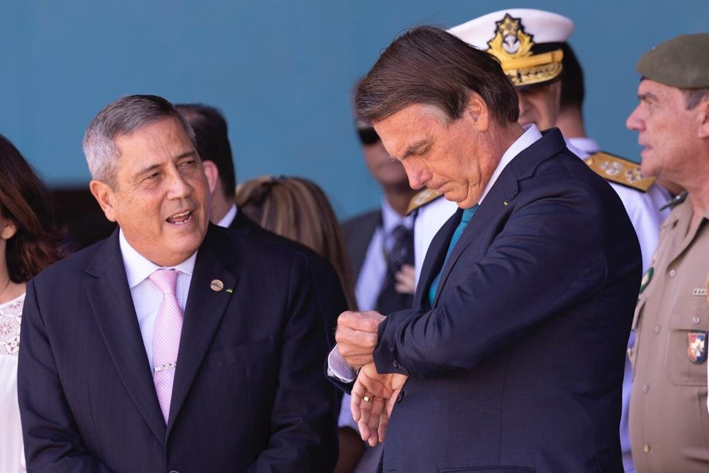 O presidente Bolsonaro conversa com o general Braga Netto, ministro da Defesa, enquanto aguardam o avião com resgatados pousar - Metrópoles
