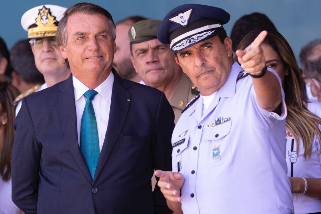 O presidente Bolsonaro conversa com o comandante da Aeuronáutica Carlos Alberto Baptista Junior, que aponta para frente enquanto aguardam o avião com resgatados pousar. Atrás, a ministra da Secretaria de Governo, Flávia Arruda, como militares - Metrópoles