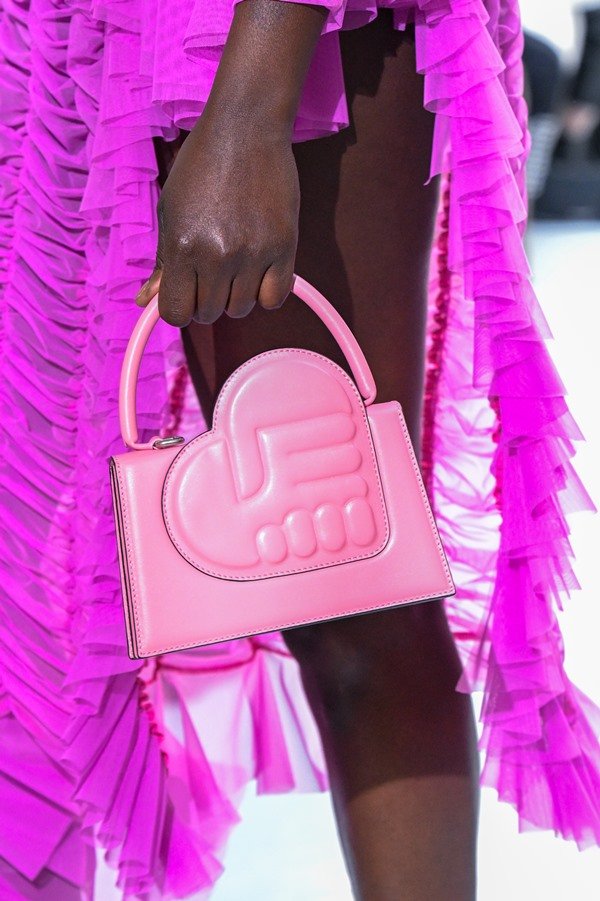Bolsa rosa sendo segurada por uma mulher. A peça é da marca Ester Manas.
