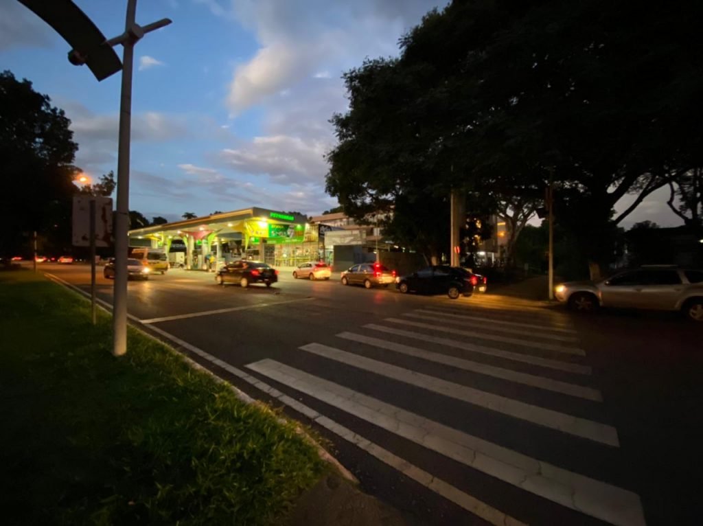 Faixa de pedestres e fila de carros em posto de combustível ao fundo