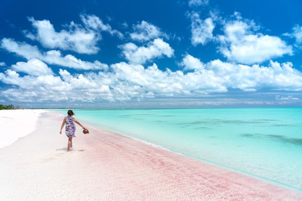 mulher caminhando em praia com areia rosa