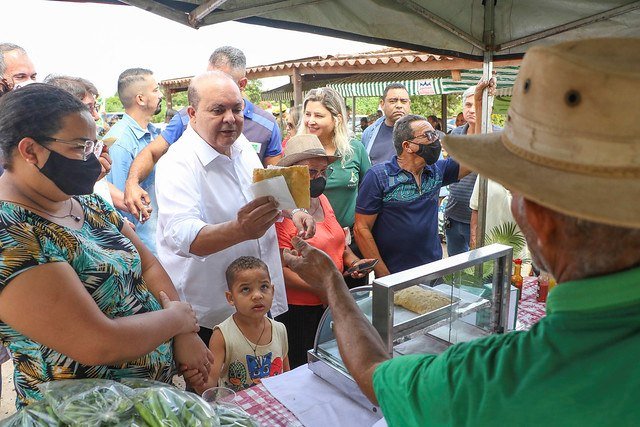 Ibaneis Rocha, de camisa branca, segura pastel. Ele está rodeado de pessoas
