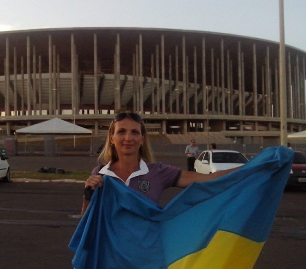 Mulher segurando bandeira azul e amarela em frente a estádio