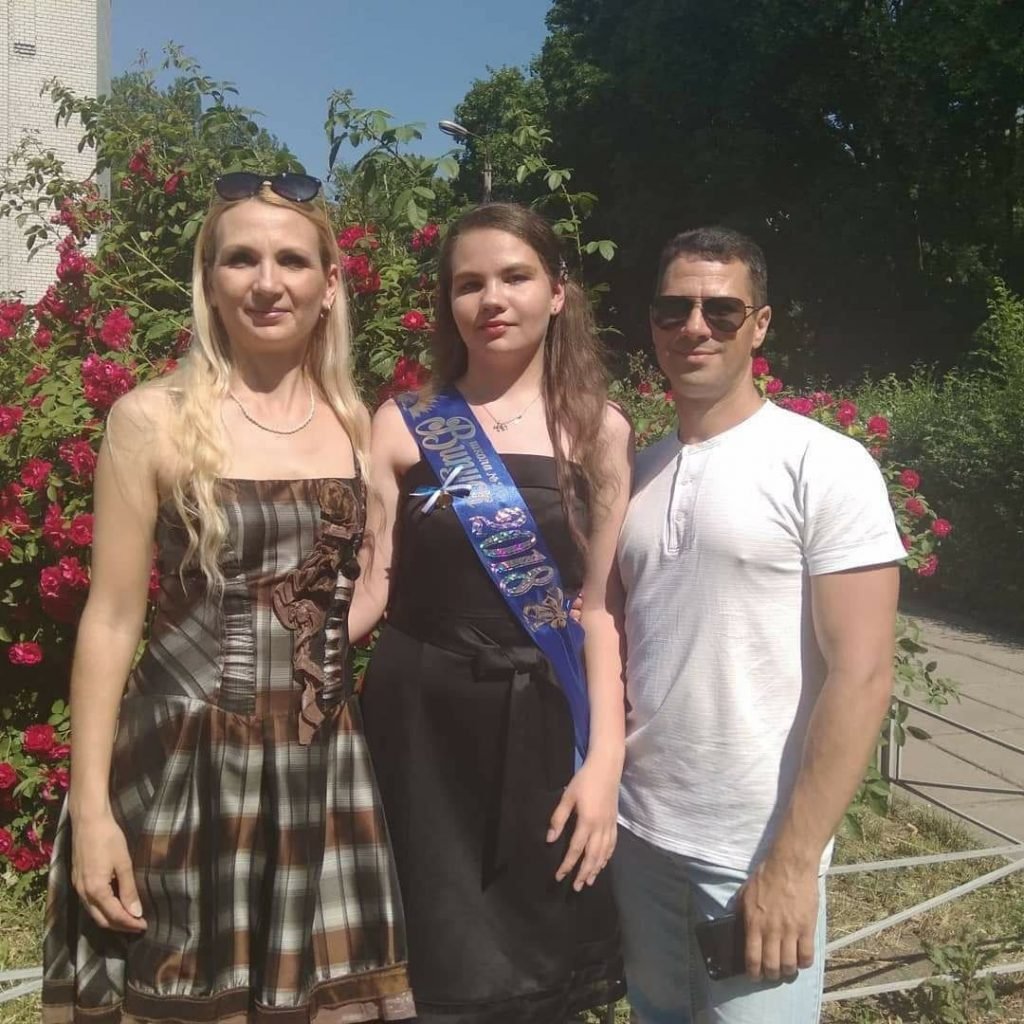 Duas mulheres e um homem em frente a flores