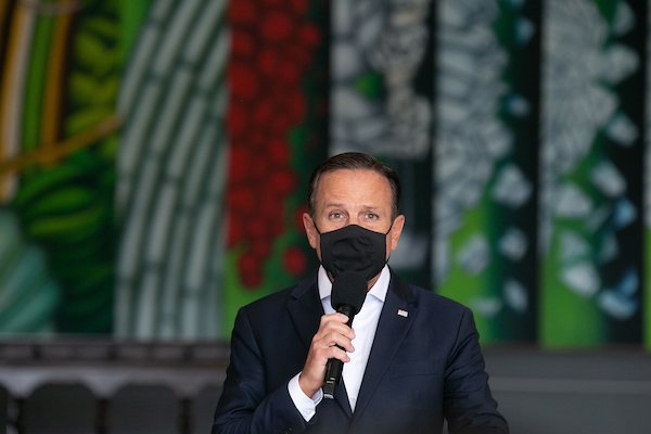 O governador de São Paulo e pré-candidato à presidência, João Dória. Ele fala num pulpito, dando entrevista coletiva, e usa máscara - Metrópoles