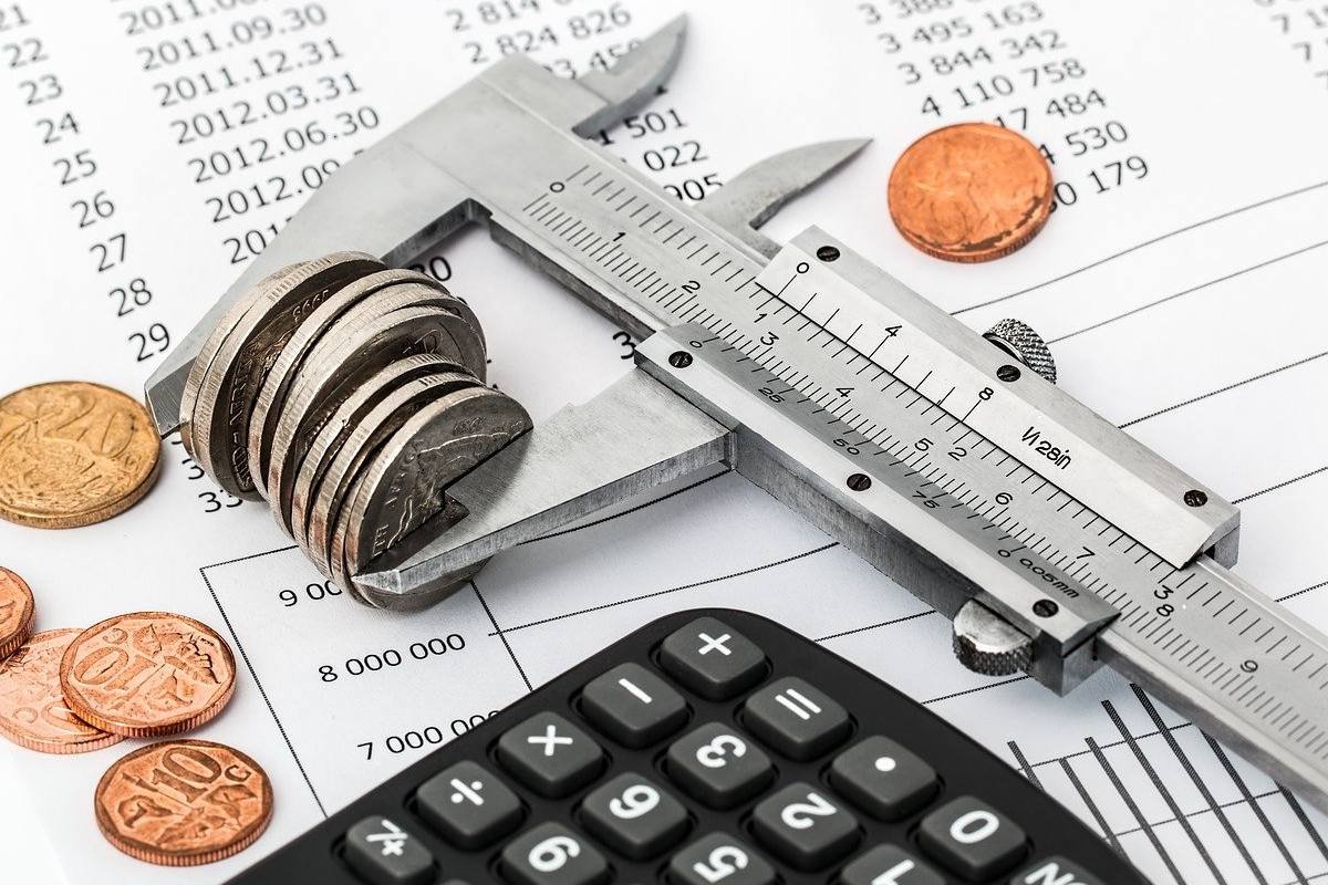 Imagem colorida de calculadora preta, régua branca e moedas sobre um papel. Ilustração de negociação de dívidas.