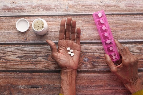 In the image, hands are resting on top of a table and holding medicine- Metropolises