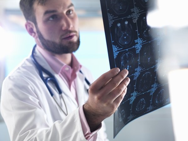 Doctor looking at CT scan.  He wears a white coat and a pink shirt underneath - metropolises