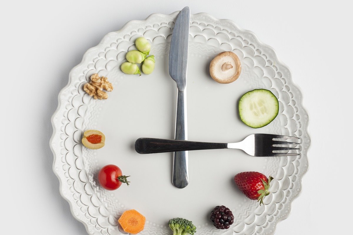 Foto mostra prato com os talheres e comidas dispostos de forma que lembra um relógio de ponteiro, ilustrando o hábito de jejum intermitente