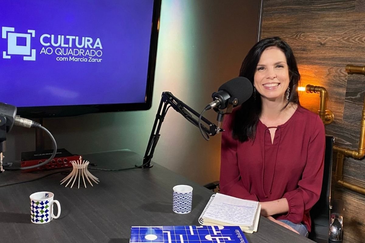 A apresentadora do podcast Cultura ao Quadrado, Márcia Zarur, sorri no cenário do programa - Metrópoles