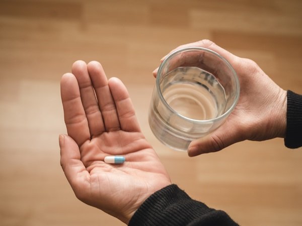 Person putting medicine in one hand and the other holds a cup - Metropolises