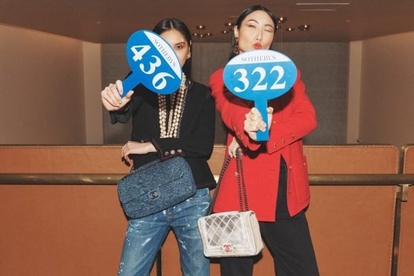 Duas mulheres usando roupas e bolsas da Chanel exibem placas de leilão - Metrópoles