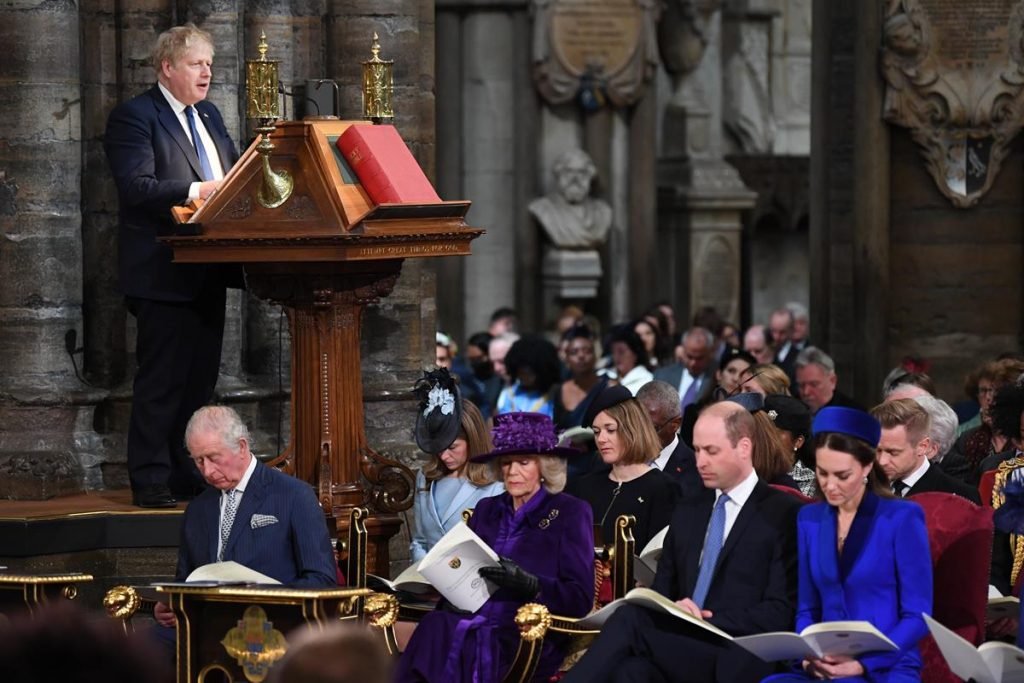 Boris Johnson, príncipe William, Camilla Parker, príncipe Charles e Kate Middleton. Boris está falando enquanto há um público sentado