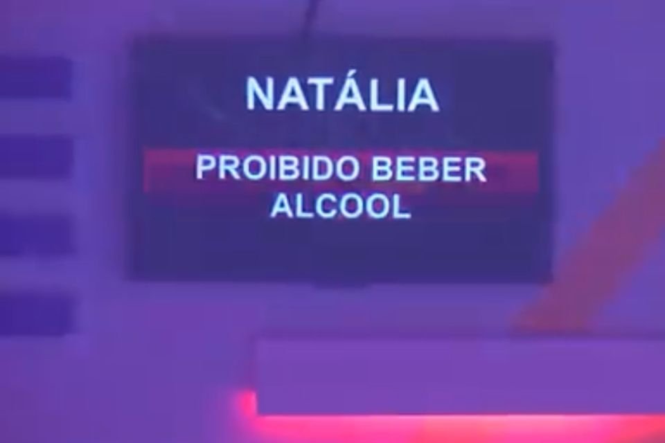 Imagem colorida mostra o momento em que a produção do BBB22 emite, através de uma tv da casa, uma ordem para Natália Deodato: ela está proibida de beber