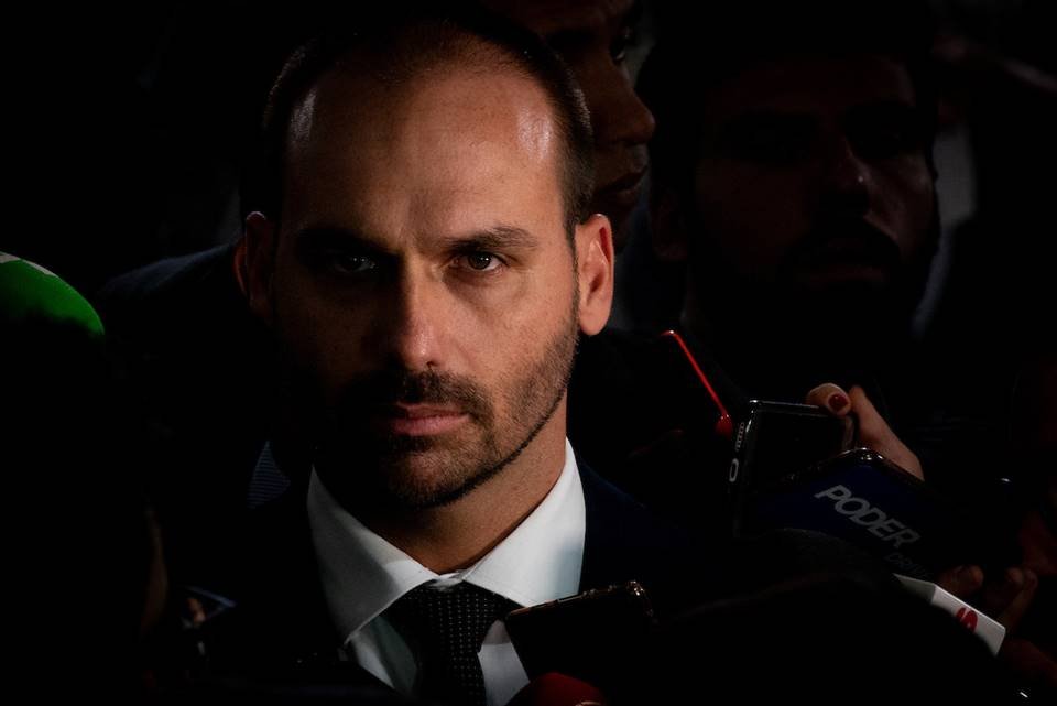 O deputado federal Eduardo Bolsonaro em entrevista coletiva. Ele olha sério para fente e usa terno, cercado por microfones - Metrópoles