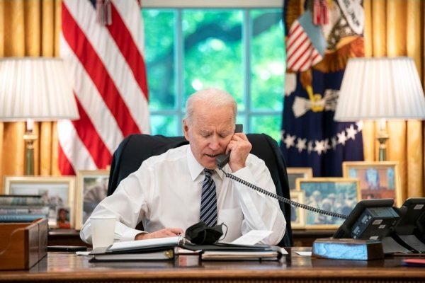 Presidente dos Estados Unidos, Joe Biden, em seu gabiente presidencial na Casa Branca. Ele está ao telefone e lê documentos em sua mesa - Metrópoles
