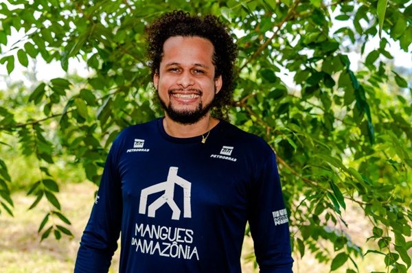 homem com camisa azul e cabelo amarrado sorri