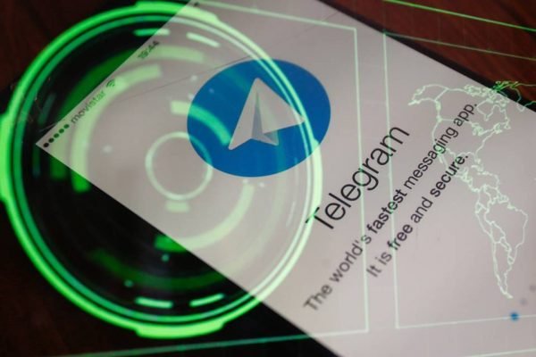 Foto de celular com app do Telegram aberto. Sobreposto, holograma verde que mostra radar e mapa-mundi - Metrópoles