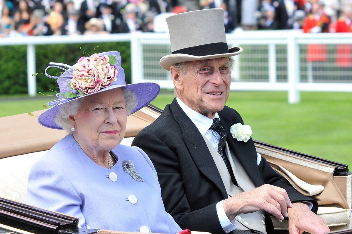 Foto colorida. O casal rainha Elizabeth e príncipe Philip estão em um carro