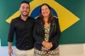 Homem e mulher posam para foto com bandeira do Brasil no fundo
