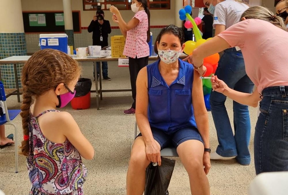 Menina olhando mulher sentada sendo vacinada