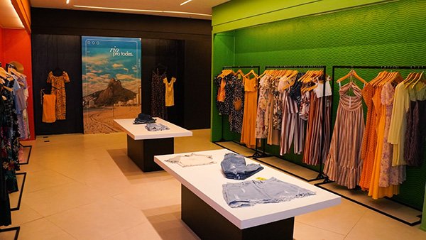 Loja da marca chinesa de roupas Shein no Brasil, no Rio de Janeiro. Na foto é possível ver araras de roupas e uma mesa com mais produtos, como shorts jeans. Uma das paredes é verde a outra possui um quadro de uma praia da capital carioca.