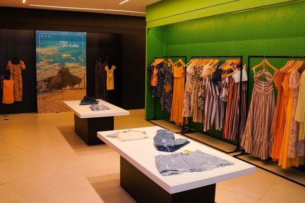 Loja da marca chinesa de roupas Shein no Brasil, no Rio de Janeiro. Na foto é possível ver araras de roupas e uma mesa com mais produtos, como shorts jeans. Uma das paredes é verde a outra possui um quadro de uma praia da capital carioca.