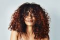 mulher com cabelos cacheados e luzes ruivas
